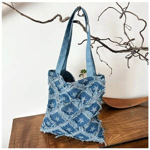 Detail of distressed denim tote bag with star patterns and raw fringe edges