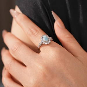 Silver ring with oval light blue gemstone and zircon halo worn on hand detail