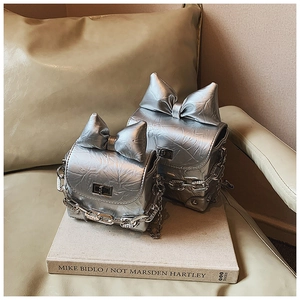 Detail silberner Plissee-Handtaschen mit Schleifendekor und Metallkettenriemen