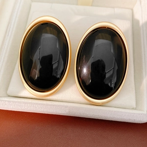 Detailed macro view of retro oval stud earrings with matte gold frames and black resin inlay