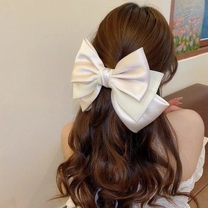 Close-up of a large layered champagne satin and chiffon bow hair clip on long wavy hair