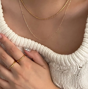 Detail shot of a minimalist knot ring and gold chain necklace on a white sweater