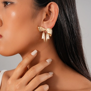 Detail of a textured golden metallic bow earring worn by a model with elegant styling