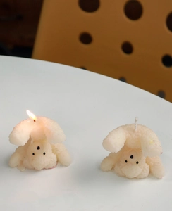 Detail of two white teddy bear scented candles, one lit and one unlit, on a white desk