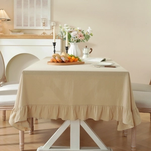 Beige washed cotton tablecloth with ruffled edges on a dining table in a cozy room