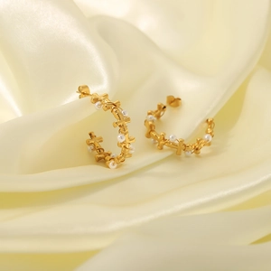 Golden C-shaped stainless steel earrings with white pearls on elegant cream silk background