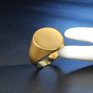 Macro view of golden matte signet ring showing brushed metal texture on a model hand