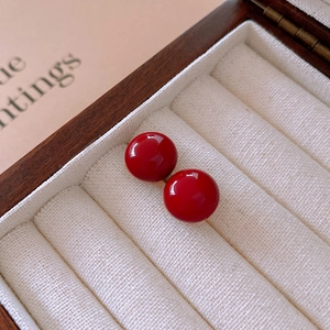 Close-up of minimalist red round stud earrings on a white velvet jewelry box slot