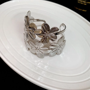 Macro shot of silver floral cuff bracelet with brushed metal texture on white ceramic tray