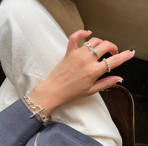 Close-up of minimalist silver beaded ring and turquoise chain rings on model fingers