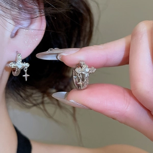 Close-up of silver zircon cross hoop earring on model showing intricate metal texture