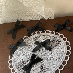 Détail de six barrettes à nœud en ruban de satin noir fait main sur fond de dentelle
