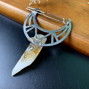 Silver crescent moon hair clip with a natural raw crystal pendant on a wood base