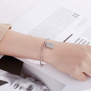 Detailed shot of silver bangle featuring a rectangular charm with engraved moon and stars