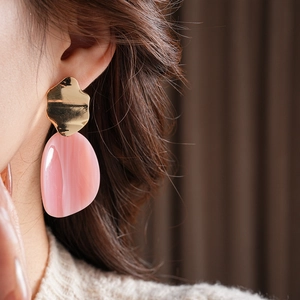 Modèle portant des boucles d'oreilles ovales irrégulières en acrylique rose et métal doré