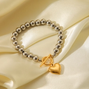 Polished stainless steel beaded bracelet with gold heart charm on silk background