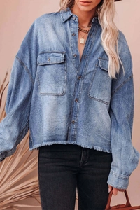 Detail view of denim shirt featuring front flap pockets and frayed raw hem design