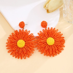 Detailed view of handmade raffia flower earrings in vibrant orange and yellow colors
