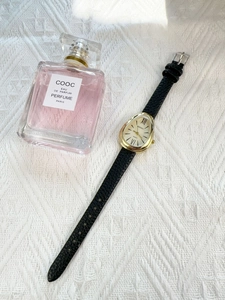 Detailed close-up of a vintage gold snake-head watch with black leather strap and perfume