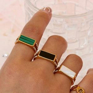 Detail of three stainless steel rings with emerald, black, and white shell gemstones