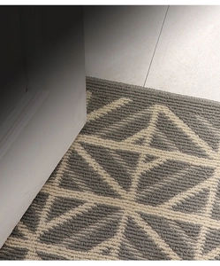 Detail of geometric entryway mat under white door showing thin profile and woven texture