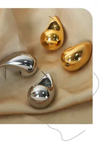 Detailed view of large polished gold and silver teardrop earrings on champagne satin fabric