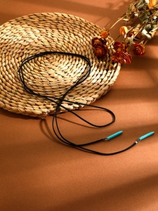 Detail of bohemian turquoise horn pendants on a black cord over woven mat with leaf shadows