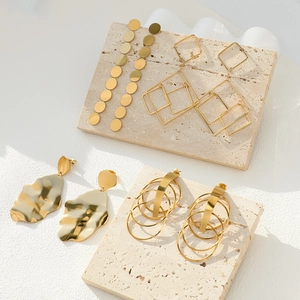 Selection of elegant gold geometric earrings displayed on a minimalist stone base