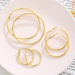 Three pairs of gold hoop earrings with twisted rope texture in various sizes on a white tray