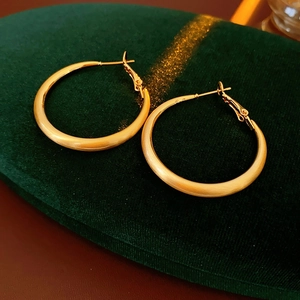 Detail of gold brushed metal hoop earrings resting on dark green velvet fabric