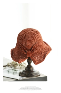 Detalle de sombrero de paja caramelo con lazo decorativo en soporte de madera vintage
