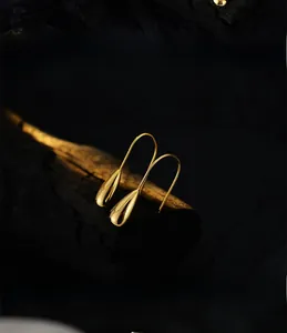 Macro shot of polished gold-plated teardrop earrings on a textured black charcoal background
