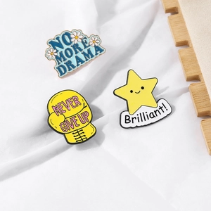 Three colorful enamel pins featuring No More Drama, Never Give Up, and Brilliant motifs