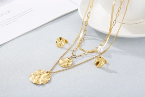 Detailed view of multilayer gold necklace with hammered disc pendants and a white pearl