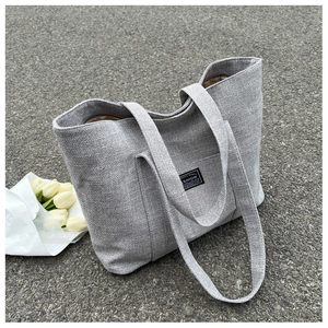 Close-up of grey canvas tote bag with fashion label on asphalt background with flowers