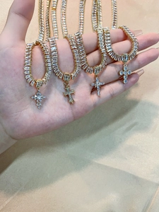 Detail of four golden cross necklaces with zircon inlays on beige silk background
