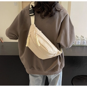 Detailed view of beige woven crossbody bag worn on shoulder by model in casual setting