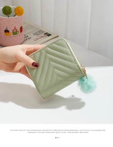 Detail of light green quilted mini wallet with pompom charm held in a person's hand