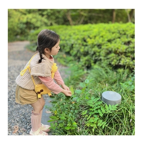 Detail of cute yellow knit giraffe crossbody bag styled on a toddler girl outdoors