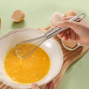 Stainless steel manual whisk stirring egg yolks in a bowl for baking preparation