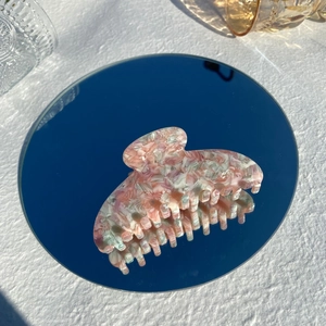 Macro detail of marbled pink and green acetate hair claw clip on a reflective mirror