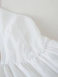 Macro view of white silky fabric with gathered pleats and detailed stitching on the dress