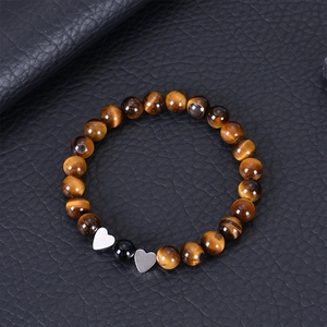 Macro detail of tiger eye beaded bracelet with heart charms on black leather background