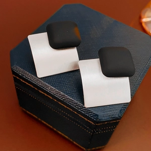 Macro shot of geometric square earrings with matte black and brushed silver texture