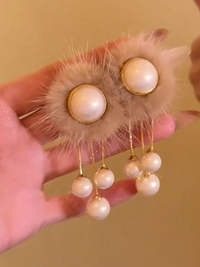 Détail de boucles d'oreilles pompons beiges avec perles blanches et longues chaînes