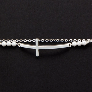 Macro shot of silver cross pendant and white freshwater pearls on a double layer bracelet