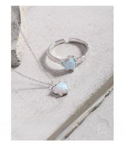 Set minimalista in argento S925 con collana e anello opale a cuore su sfondo grigio