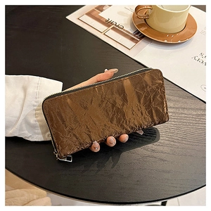 Detail of dark brown crinkled texture long wallet with gold zipper on wooden desk