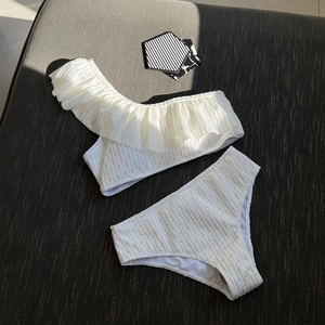 White ruffle one-shoulder bikini set with textured dot fabric on dark grey background