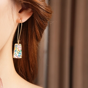 Dettaglio di orecchino vintage dorato con motivo astratto in smalto colorato